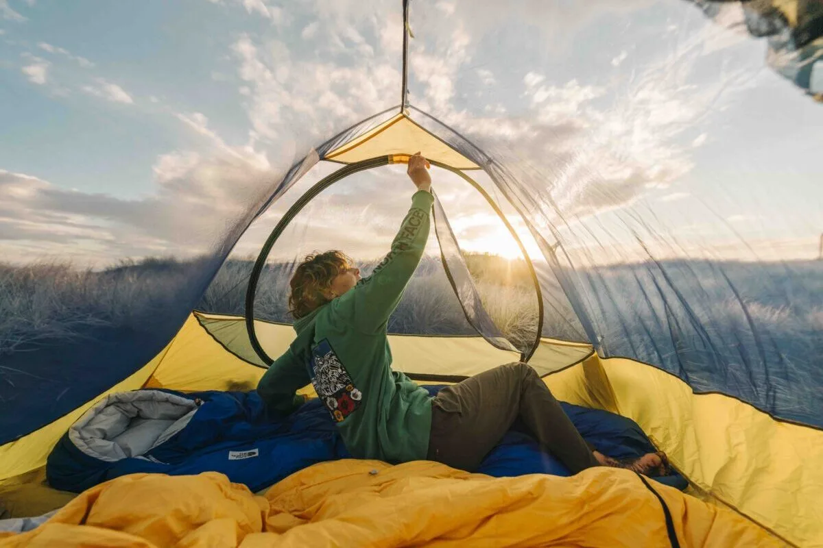 A camper opening a The North Face tent at sunrise